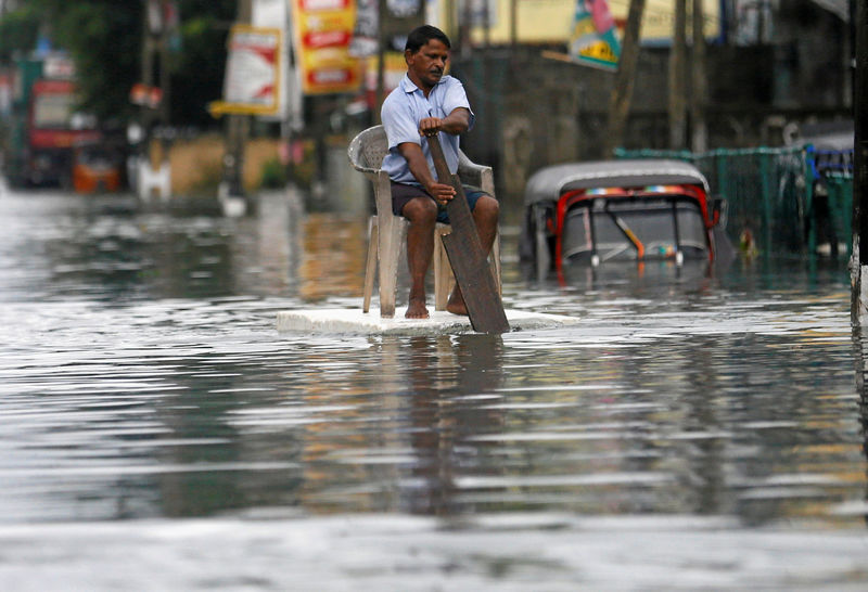 © Reuters. A man sits on a chair as he uses a piece of styrofoam to move through a flooded road in Wellampitiya