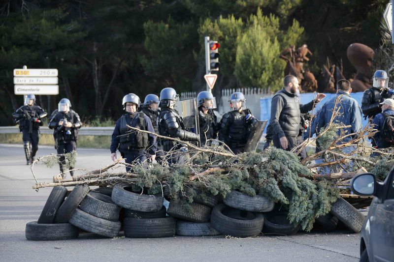© Reuters. French gendarmes stand near branches, wood pallettes and tyres after striking workers blocked roads near the oil refinery at Fos-sur-Mer