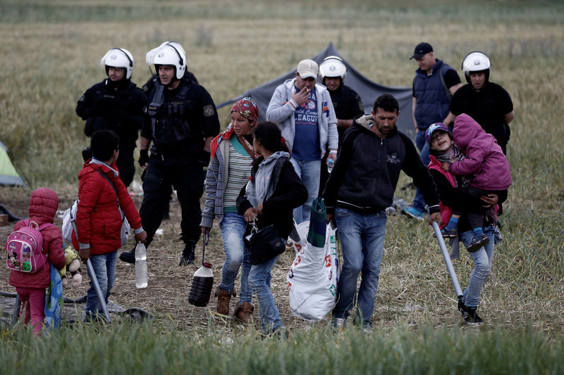 © Reuters. Família refugiada deixando acampamento de Idomeni, na Grécia, ao lado de policiais