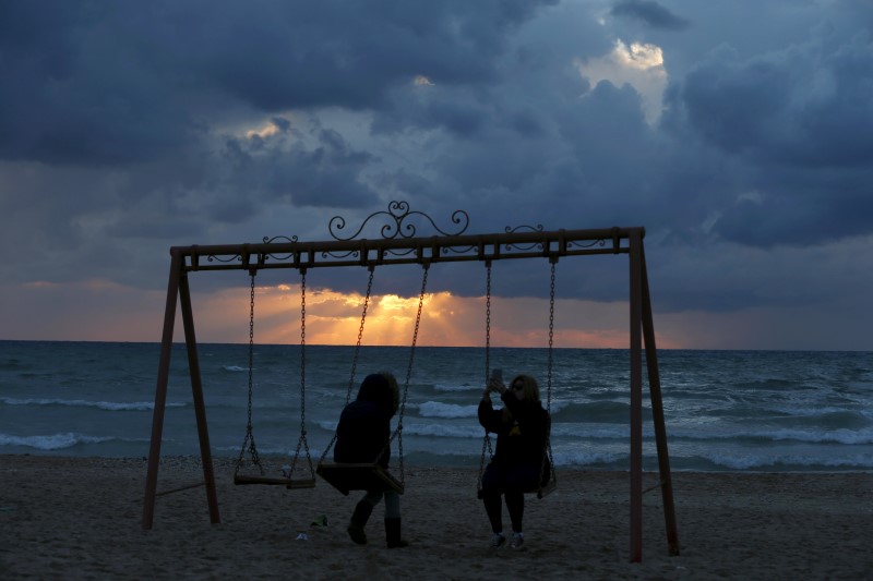 © Reuters. A woman takes a selfie on a swing at the seaside of Ramlet al-Bayda beach as storm clouds loom during sunset in Beirut