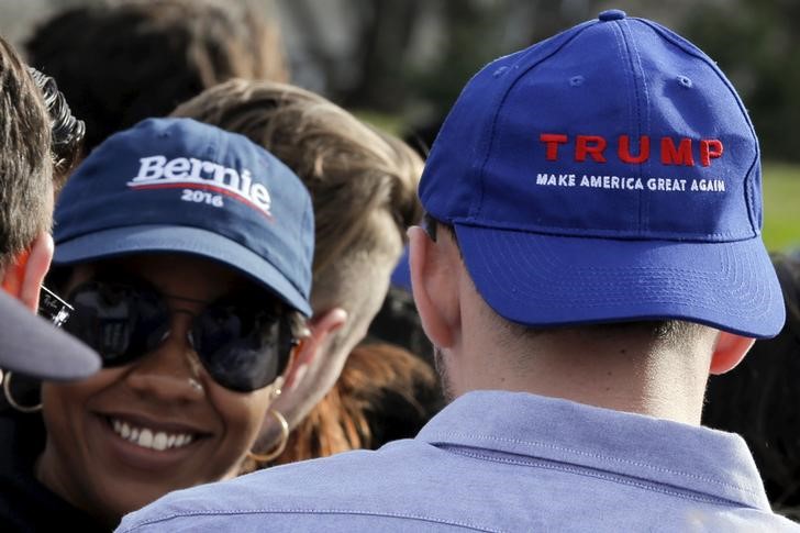 © Reuters. A woman wearing a hat with the word "Bernie" smiles towards a man wearing a hat stating "Trump" as they stand in line-up to take part in a campaign rally for U.S. Democratic presidential candidate Bernie Sanders at Saint Mary's Pa