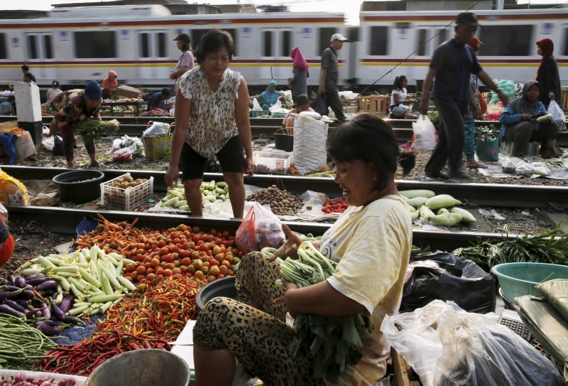 © Reuters. A vendor serves a customer at a vegetable market as a commuter train passes in Jakarta