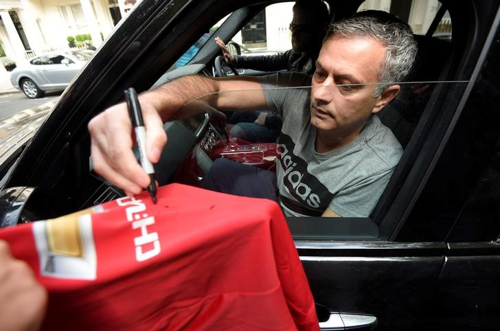 © Reuters. Mourinho signs a Manchester United soccer shirt held out by a fan as he leaves his house in London