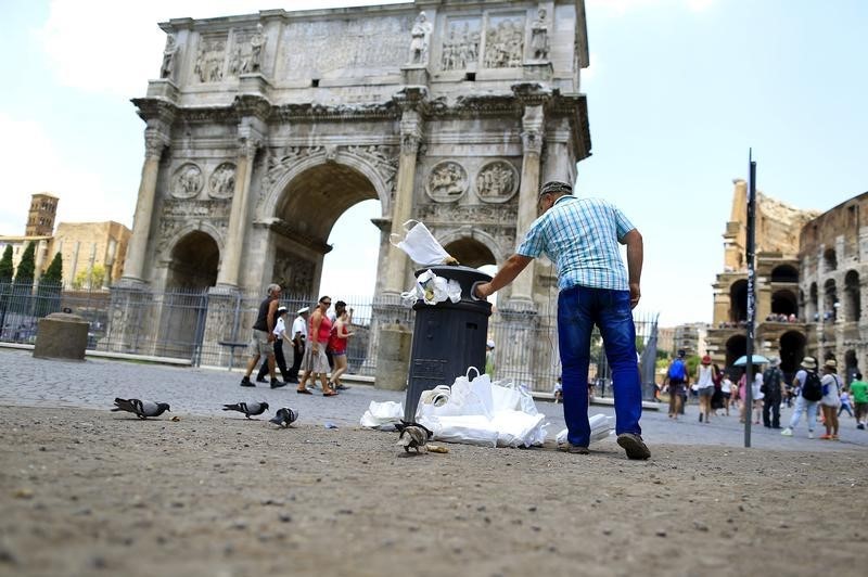 © Reuters. A man tries to put rubbish in a full garbage bin in front of the Arch of Constantine in Rome