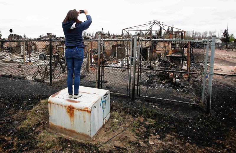 © Reuters. A woman takes photos of the burned remains of a house in the Abasand neighbourhood of Fort McMurray