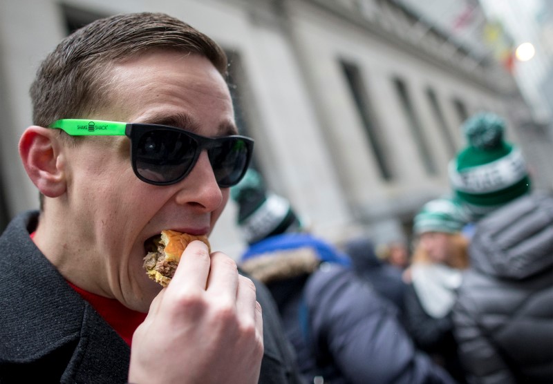 © Reuters. Robby Keesb eats a Shake Shack burger  in front of New York Stock Exchange as part of the company's IPO celebration