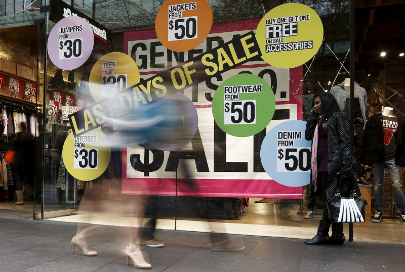 © Reuters. A woman uses her mobile phone in front of sale signs in the window of a clothes store at a shopping mall in central Sydney