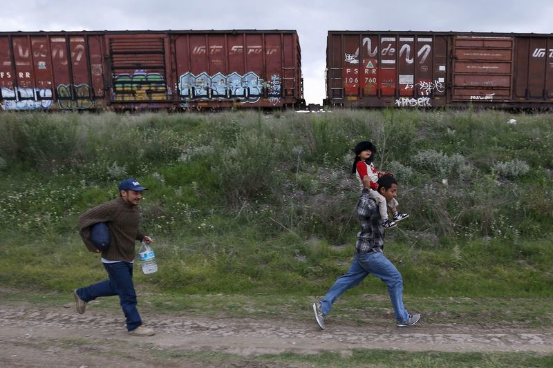 © Reuters. A Salvadoran father carries his son while running next to another immigrant as they try to board a train heading to the Mexican-U.S. border, in Huehuetoca