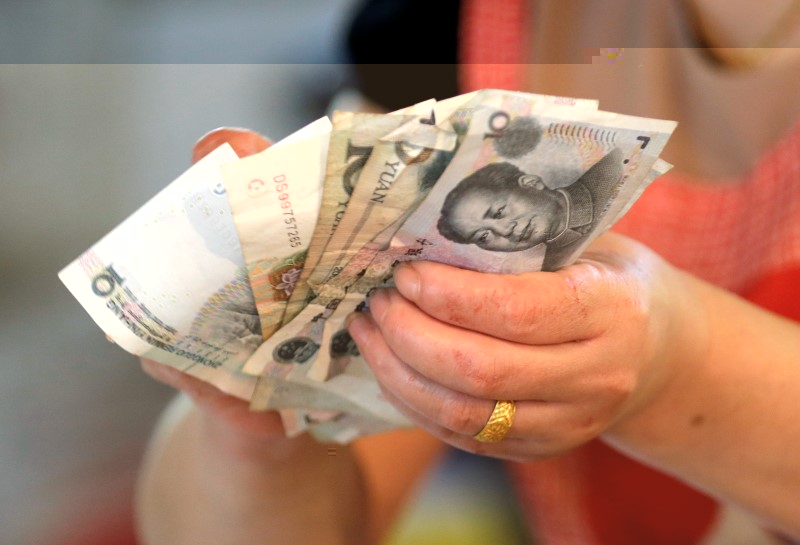 © Reuters. A vendor holds Chinese yuan notes at a market in Beijing