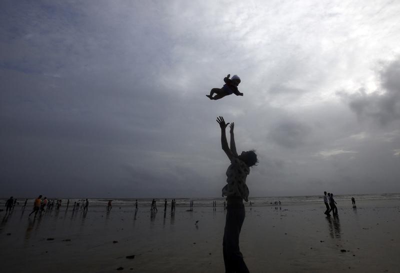 © Reuters. A man plays with his child against the backdrop of monsoon clouds on a beach in Mumbai