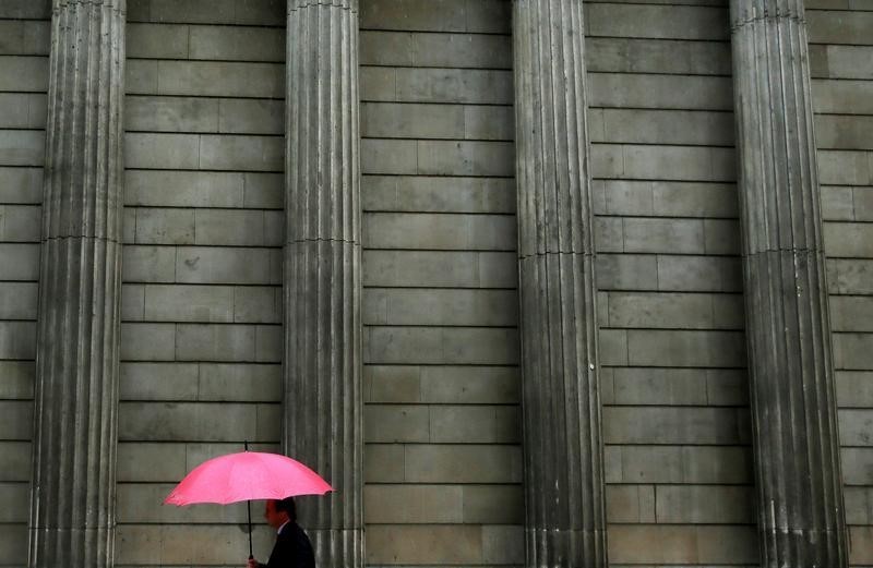 © Reuters. A man holding an umbrella walks past the Bank of England in the City of London