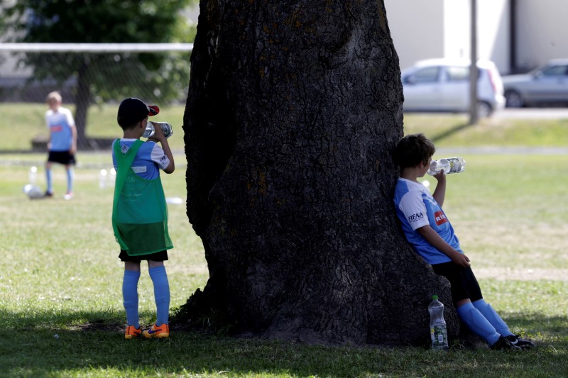 © Reuters. Children rest in the shadow of an oak in the middle of  soccer pitch in Orissaare