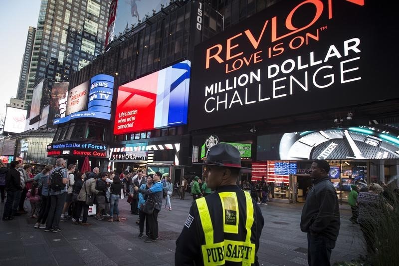 © Reuters. A Public Safety officer keeps watch as people stand in front of  a billboard owned by Revlon that takes their pictures and displays them in Times Square in the Manhattan borough of New York