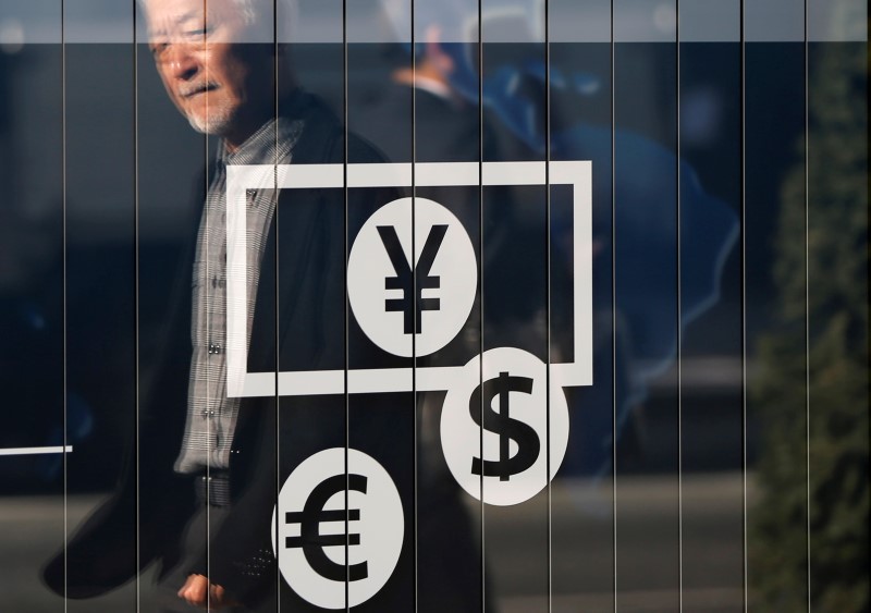 © Reuters. Passers-by are reflected on a signboard displaying currency signs outside a bank in Tokyo