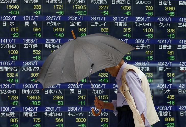 © Reuters. A pedestrian holding an umbrella walks past a stock quotation board outside a brokerage in Tokyo