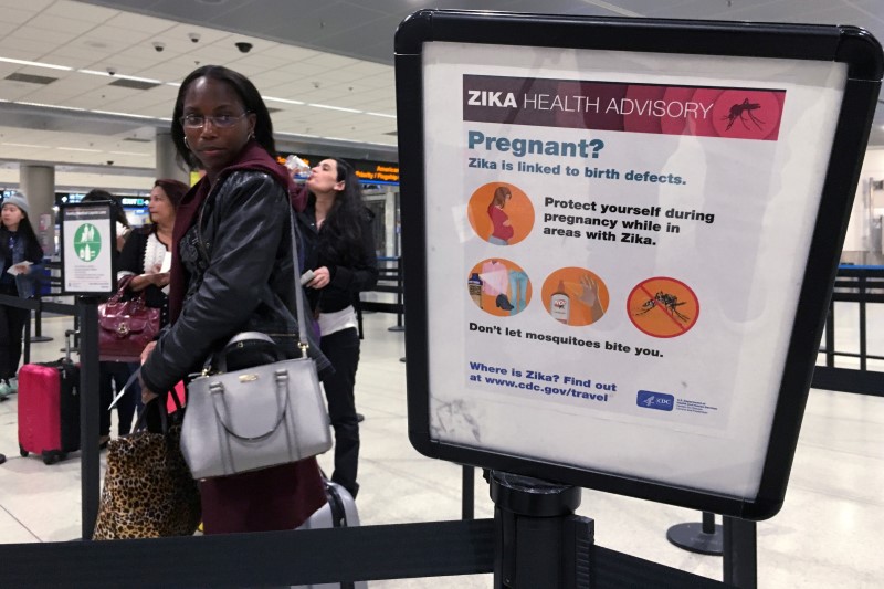 © Reuters. A woman looks at a Center for Disease Control (CDC) health advisory sign about the dangers of the Zika virus as she lines up for a security screening at Miami International Airport in Miami