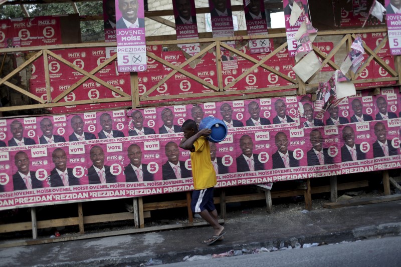 © Reuters. A man carrying a gas cylinder walks next to electoral posters of presidential candidate Jovenel Moise in Port-au-Prince, Haiti