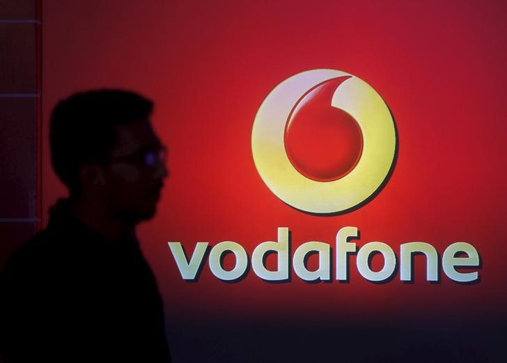 © Reuters. A man casts silhouette onto an electronic screen displaying logo of Vodafone India after a news conference to announce the half year results in Mumbai