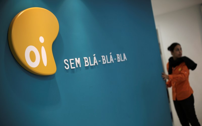 © Reuters. A woman stands next to the logo of Brazil's largest fixed-line telecoms group Oi, inside a shop in Sao Paulo