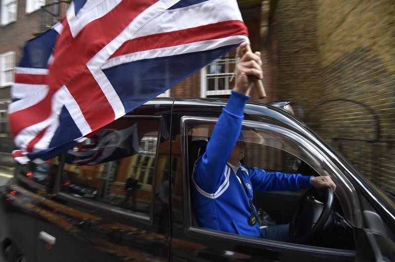 © Reuters. A taxi driver holds a Union flag, as he celebrates following the result of the EU referendum, in central London