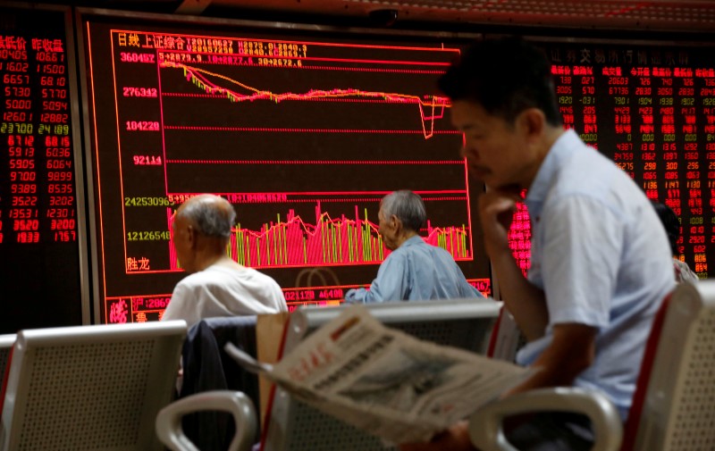 © Reuters. A man reads a newspaper in front of an electronic board at a brokerage house in Beijing