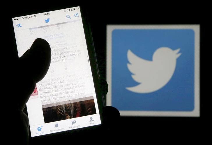 © Reuters. Homem lê tuítes no celular em frente a tela com logo do Twitter, em Bordeaux