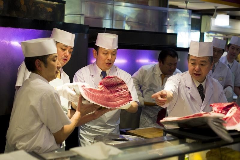 © Reuters. Chefs of the sushi restaurant chain Sushi Zanmai hold a freshly cut piece of a blue fin tuna at the chain's main restaurant at the outer Tsukiji market in Tokyo