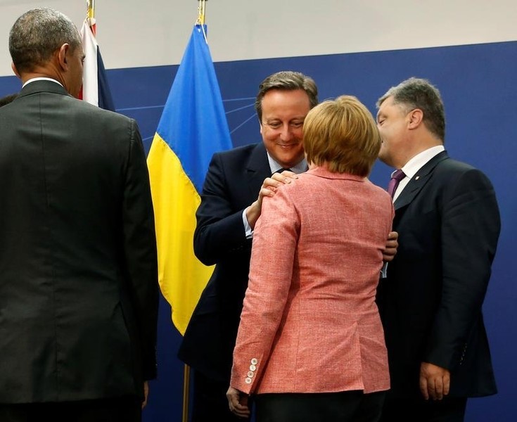 © Reuters. Cameron embraces Merkel after a photo call with fellow NATO leaders, including Obama and Poroshenko, alongside the NATO Summit in Warsaw, Poland