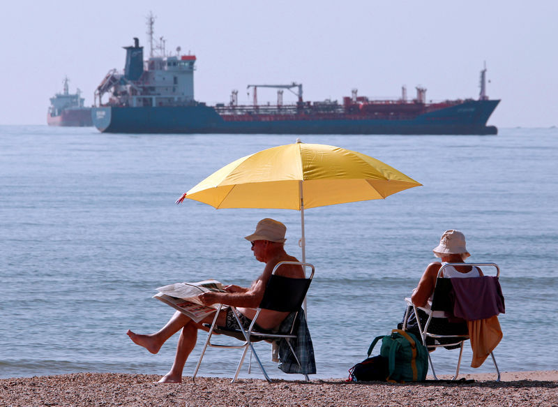 © Reuters. People sunbathe as oil and gas tankers are anchored off the Fos-Lavera oil hub near Marseille
