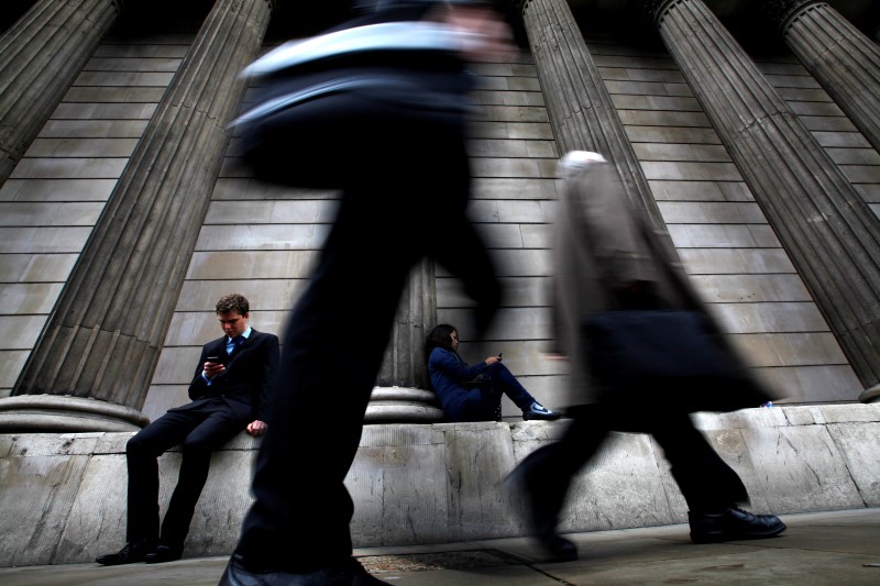 © Reuters. A man and woman use their mobile phones as commuters walk past the columns of the Bank of England in the City of London