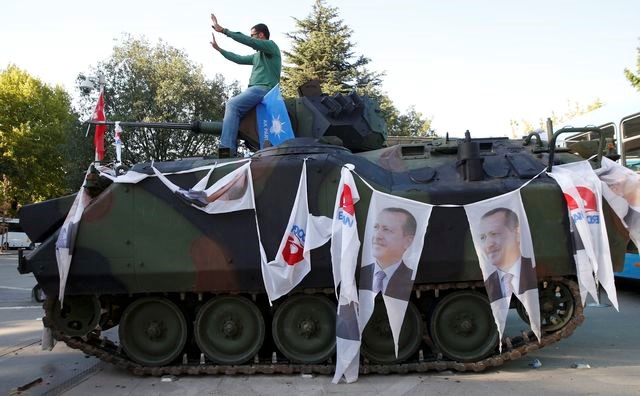 © Reuters. A man poses on an Armored Vehicle with portraits of Turkish President Tayyip Erdogan parked outside the parliament building in Ankara