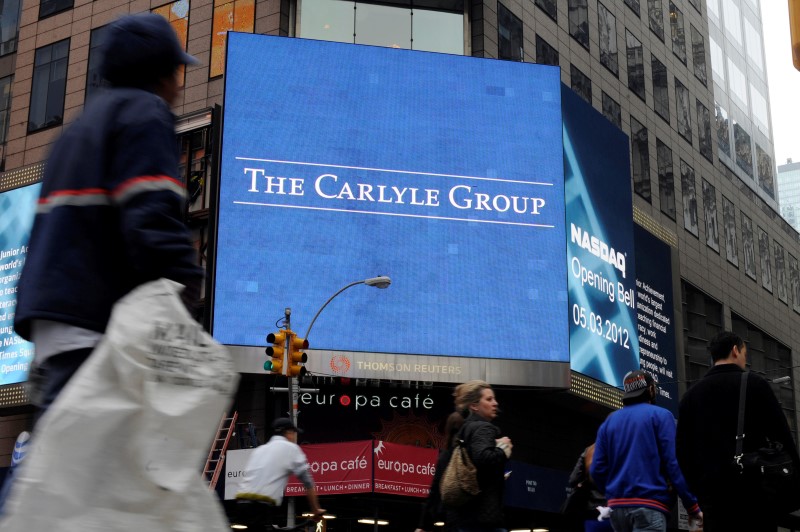 © Reuters. Passersby walk in front of video monitors announcing the Carlyle Group's listing on the NASDAQ market site in New York's Times Square after the opening bell for trading