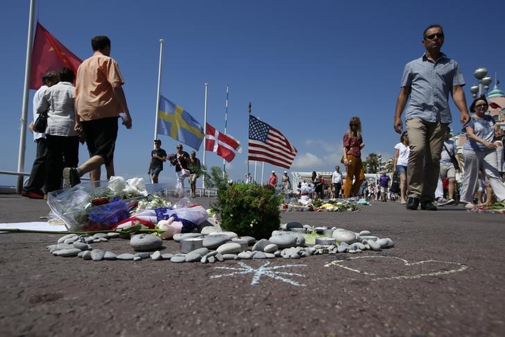 © Reuters. People walk past a heart shape makeshift memorial with a US flag placed on the road in tribute to victims before a minute of silence on the third day of national mourning after the truck attack along the Promenade des Anglais