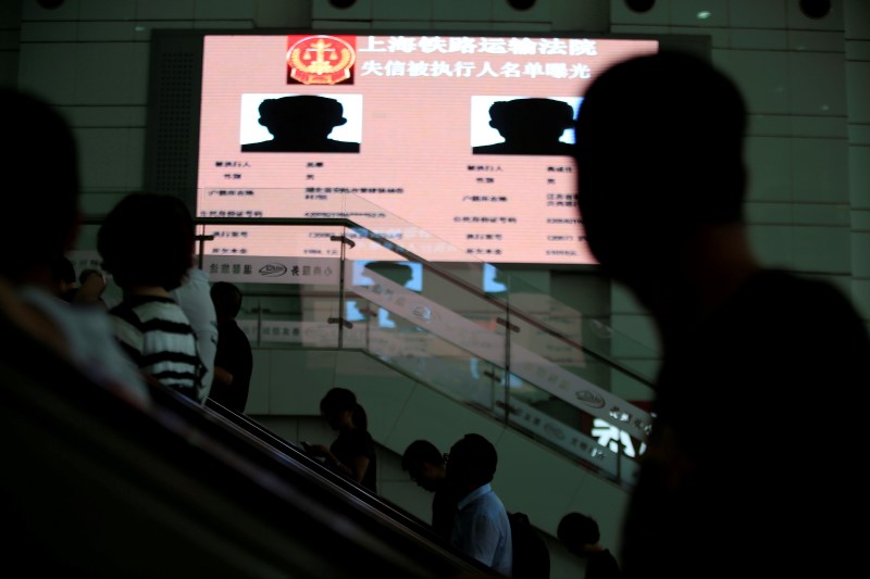 © Reuters. People standing on escalators pass a electronic screen showing information of  runaway debtors at Shanghai railway station in Shanghai