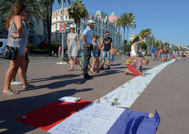 © Reuters. People write messages on a long sheet of paper on the third day of national mourning to pay tribute to victims of the truck attack along the Promenade des Anglais on Bastille Day