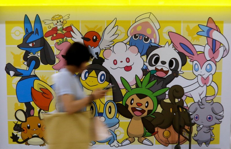 © Reuters. A woman using a mobile phone walks past a shop selling Pokemon goods in Tokyo