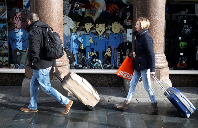 © Reuters. People pull suitcases past a shop selling Beatles merchandise in Liverpool northern England