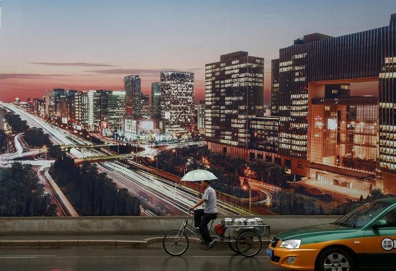 © Reuters. A man rides a tricycle past an advertising poster showing a night-time city view in Beijing,