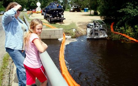 © Reuters. Local residents watch from a bridge as a tanker truck skims oil from the top of the water from the Kalamazoo River