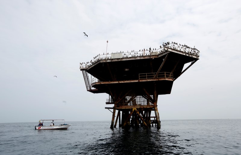 © Reuters. An abandoned oil platform is seen near tourists at Organos beach in Piura, Peru