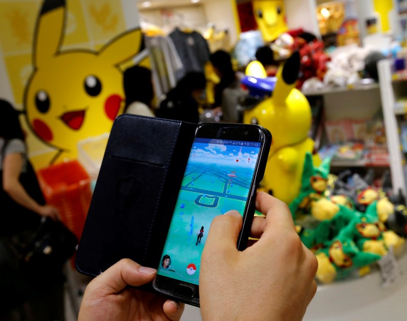 © Reuters. A man plays the augmented reality mobile game "Pokemon Go" by Nintendo in front of a shop selling Pokemon goods in Tokyo