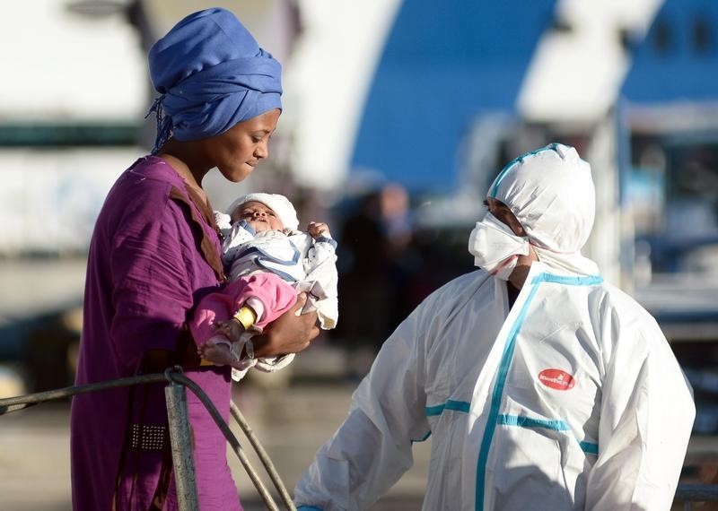 © Reuters. Una donna migrante con il suo bambino appena sbarcata a Palermo viene soccorsa