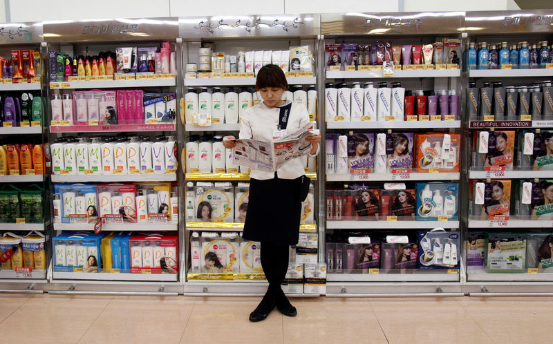 © Reuters. A saleswoman reads a newspaper as she waits for customers in front of hair products at a supermarket in Seoul