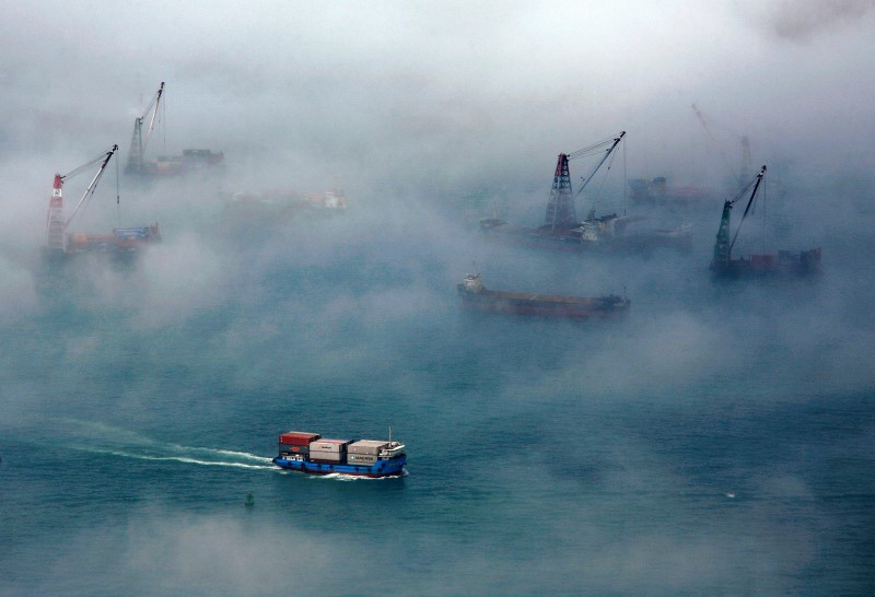 © Reuters. A container ship sails past barges during foggy conditions at Hong Kong's Victoria Harbour