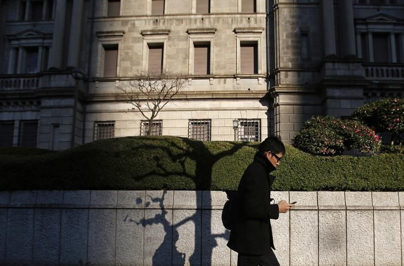 © Reuters. A man using his mobile phone walks past the Bank of Japan headquarters building in Tokyo
