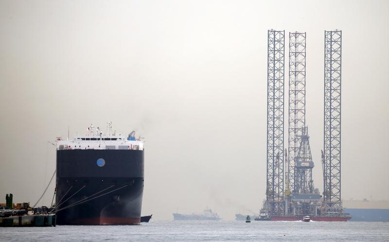 © Reuters. Part of offshore rig is towed past car carrier docked at Singapore port