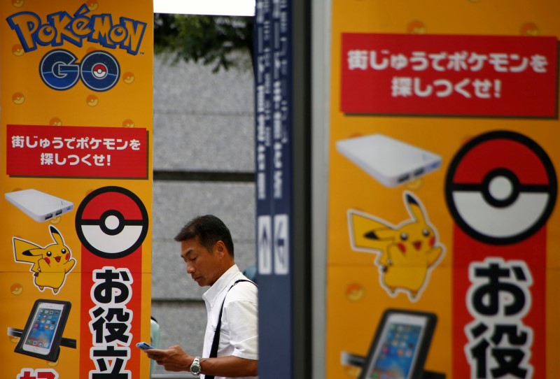 © Reuters. A man uses a mobile phone in front of an advertisement board bearing the image of Pokemon Go at an electronic shop in Tokyo