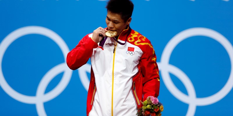 © Reuters. China's Xiaojun Lu bites his gold medal at the podium of the men's 77Kg weightlifting competition at the ExCel venue at the  London 2012 Olympic Games