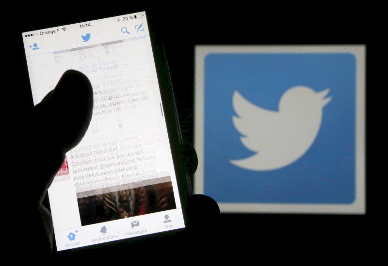 © Reuters. Un hombre lee mensajes a través de la red social Twitter en su teléfono frente al logo de la compañía en Burdeos, al suroeste de Francia