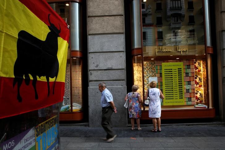 © Reuters. Women windowshop as a man walks next to a Spanish flag with a bull on it in downtown Madrid